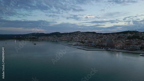 A coastal town at dusk, with boats in the harbor and a hill overlooking the buildings.