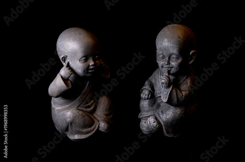 Two miniature monk statues covering ears and mouth on dark background concept see no evil hear no evil