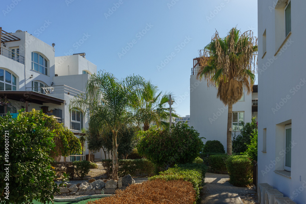 Fototapeta premium Sunny day in a tranquil residential complex with lush gardens and palm trees.