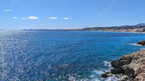 Stunning view of the Azure Coastline in Nice, France. The Mediterranean Sea glistens under a clear sky, seen from rocky shores on a sunny day