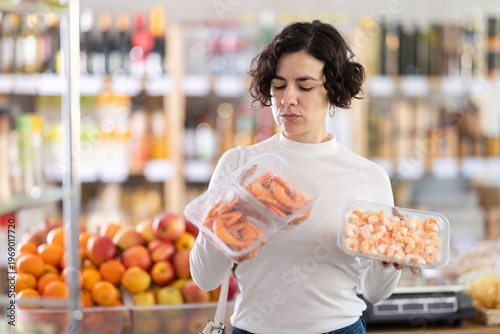 Tableau sur toile Woman buyer doubts and hesitates, chooses and select prawn in supermarket