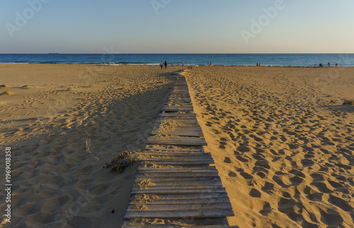 Serene wooden pathway leading to the tranquil shoreline at golden hour.