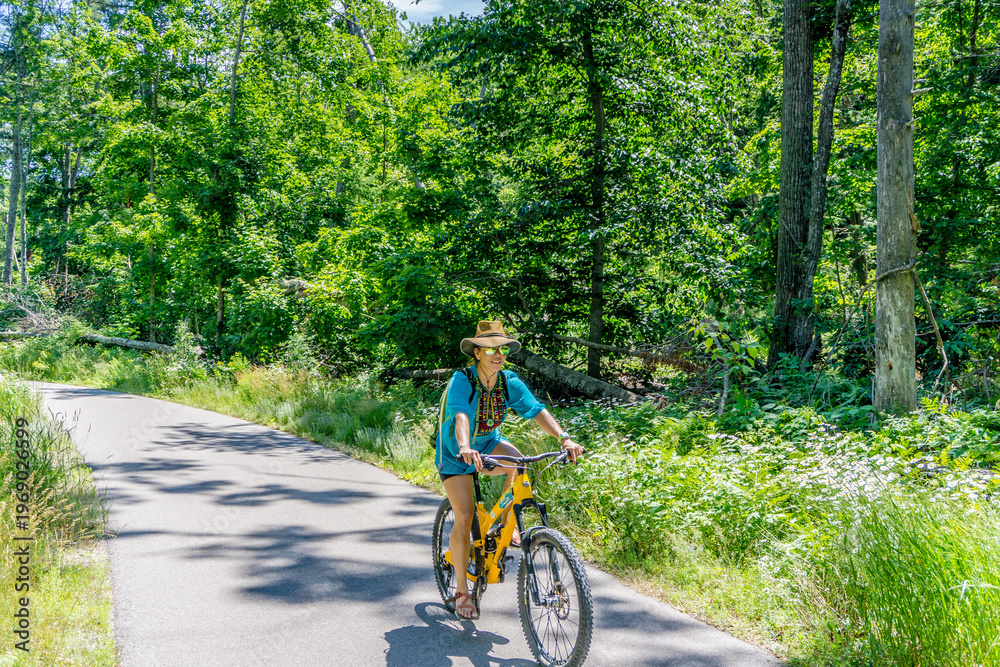 Fototapeta premium Woman rides yellow bike through sunlit forest path