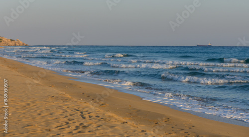 Waves gently lap at the sandy shore under a tranquil sky during sunset near an ocean coastline.