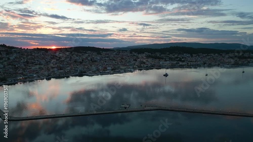 A coastal town at sunset, with the sun peeking over the horizon, reflected in the calm water.