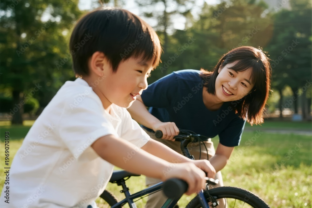 Obraz premium A woman helps a young boy learn to ride a bicycle in a sunny park.