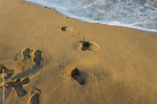 Footprints on a golden beach at sunset, where gentle waves caress the shore.