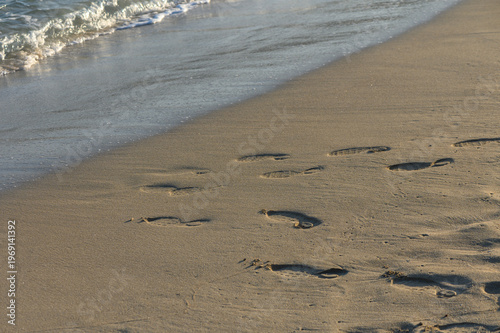 Footprints lead to the gentle waves on a serene sandy beach at sunset, capturing a moment of solitude.