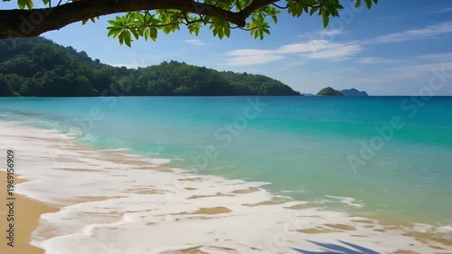 Serene Tropical Beach With Turquoise Waves Rolling Onto Golden Sand And Lush Island Background Under Clear Blue Sky