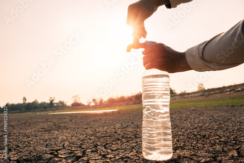 Fotografija Water scarcity concept, Filling plastic bottle from faucet in dry cracked land at sunset