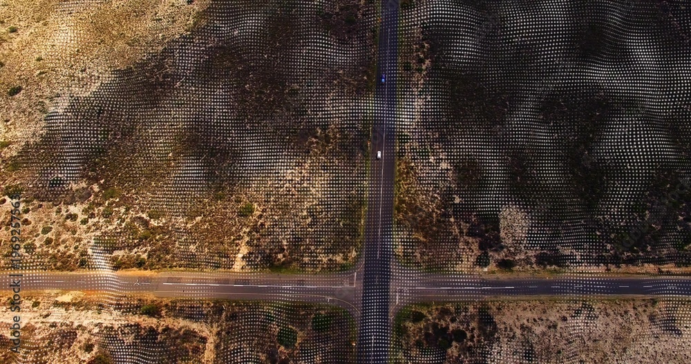 Fototapeta premium Showing four-way paved intersection crossing arid scrubland with grid markers and light vehicle
