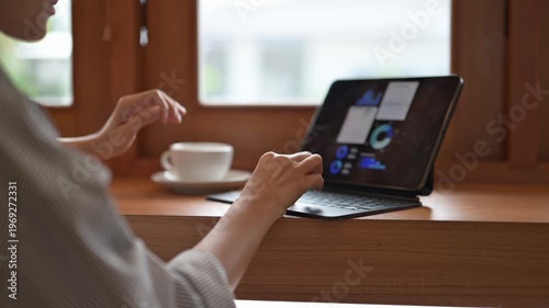 A woman is sitting at a table with a laptop and a cup of coffee. She is typing on the laptop and sipping her coffee. Concept of productivity and relaxation