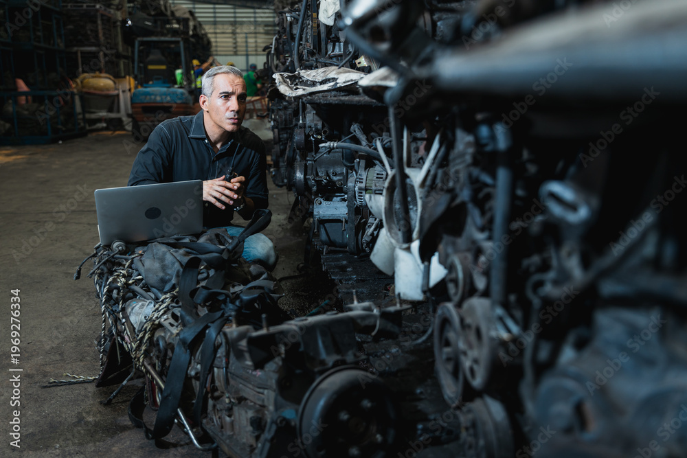 Fototapeta premium Supervisor with laptop inspecting used car engines in automotive spare parts warehouse