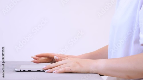 Woman is typing on a cell phone. She is wearing a white shirt. The phone is on a table