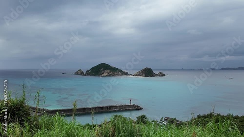 渡嘉敷島・阿波連漁港を見下ろす風景 曇天でも輝くエメラルドグリーンの海とハナリ島 動画素材 4K