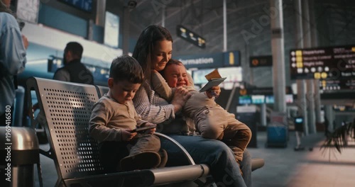 Stressed Mother Tries to Soothe Crying Infant on Terminal Benches, Older Son Sits Distracted by Smartphone. Traveling With Children, Parental Exhaustion, and Digital Devices in Managing Family Stress.