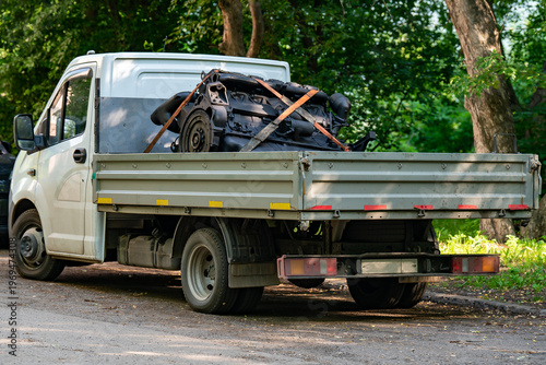 White Flatbed Truck Carrying Salvaged Car Engine Strapped On Cargo Bed Parked By Trees