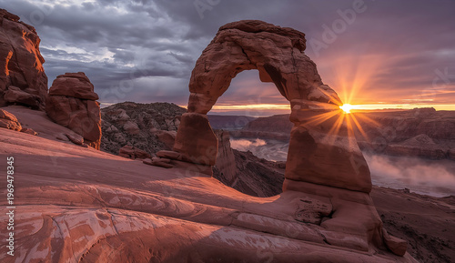 Sunset at Delicate Arch, Utah, with the sun casting warm light through the natural stone arch. The sky is partly cloudy, creating a serene atmosphere.