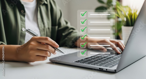Person completing a checklist while working on a laptop and taking notes