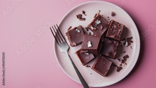 Top view of gourmet dark chocolate fudge squares served on a minimalist pink plate with a silver fork for a luxurious dessert presentation on pastel background