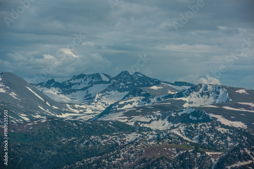 Aerial view to forest hills and big mountain range with snow, sharp rocks, po...