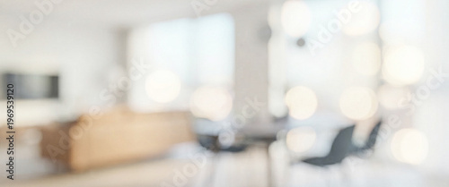 A blurred interior view of a modern living room with large windows, natural light, and contemporary furnishings, creating a warm and inviting atmosphere.