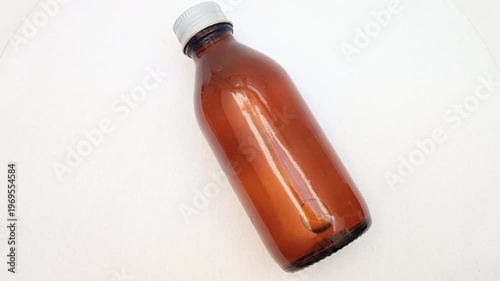 Amber glass bottle with cap rotating on white background, brown glass bottle for pharmaceuticals, syrups, essential oils, and cosmetics