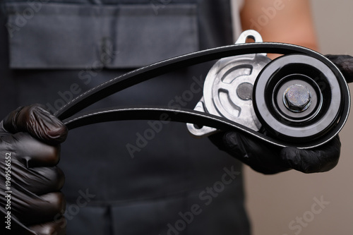 Mechanic Hands Holding Belt Tensioner In Closeup. Serpentine Belt And Pulley Assembly, Uniformed Technician Performing Inspection And Replacement. Vehicle Repair Concept