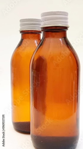 Amber glass bottles with cap rotating on white background, brown glass bottles for pharmaceuticals, syrups, essential oils, and cosmetics, vertical clip