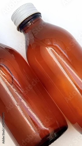 Amber glass bottles with cap rotating on white background, brown glass bottles for pharmaceuticals, syrups, essential oils, and cosmetics, vertical clip