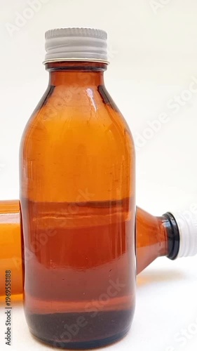 Amber glass bottles with cap rotating on white background, brown glass bottles for pharmaceuticals, syrups, essential oils, and cosmetics, vertical clip