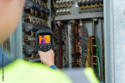 фотографія Engineer uses a thermal camera to inspect wiring inside an electrical control cabinet, supporting condition monitoring, preventive maintenance, safety checks, and fault detection