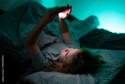 Bild auf Leinwand Kid scrolling phone under blanket at night