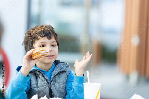 Young boy eating sandwich talking making hand gesture
