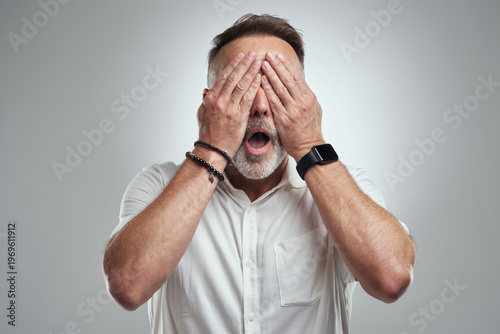 Φωτογραφία Mature, man and cover with eyes for fear, terror or shock on a white studio background