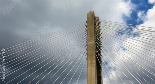 Modern cable-stayed bridge tower reaching towards a dramatic cloudy sky