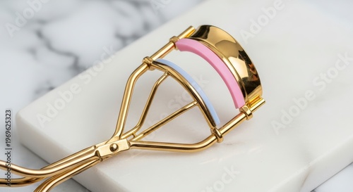 Golden eyelash curler on marble surface.