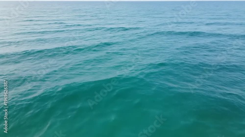 Calm ocean waves gently rolling towards the shore, showcasing a serene seascape with clear blue water and soft ripples under a bright sky