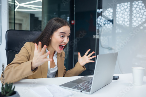 Excited cheerful young business woman using laptop computer at office getting good news, feeling happiness win lottery