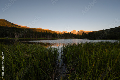 Sprague Lake reflecting forested mountain peaks under a sunset sky