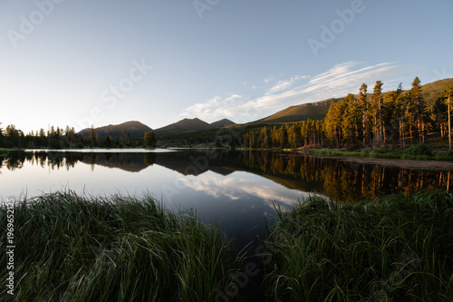 Peaceful mountain lake reflecting blue skies and forest at sunrise