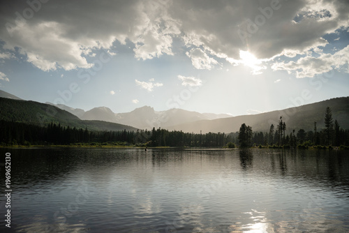 Hazy sun shining over the mountains and a still lake in the Rockies