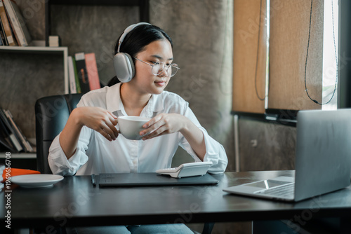 A focused young woman wearing headphones works on her laptop in a stylish home office environment.