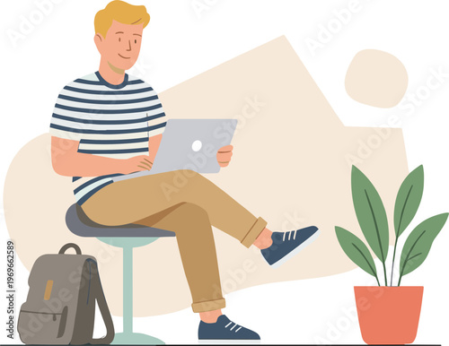 A young man sits on a stool with a laptop on his lap in a relaxed indoor setting.