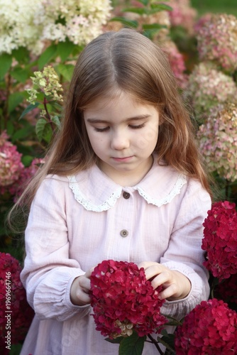 Little Girl in Vintage Pink Dress Enjoys the Beauty of Hydrangeas in a Garden. Moment of Serene Joy.