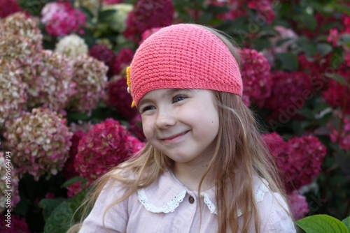 Portrait of Adorable Little Girl in Pink Hat Surrounded by Beautiful Hydrangeas in Autumn Garden.