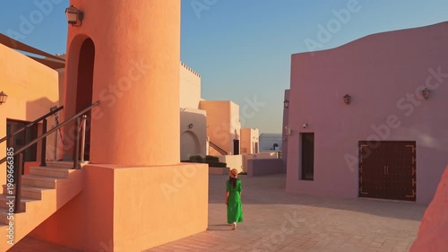 Doha, Qatar - 8th january, 2026:Woman tourist walking stand near traditional tower in Mina District Doha with pastel buildings and long shadows showcasing modern Middle East urban design