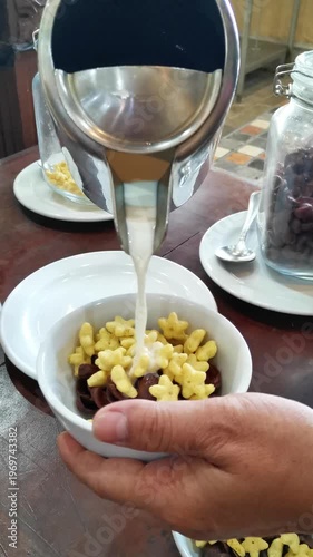 Pouring Fresh Milk from a Stainless Steel Pitcher into a Bowl of Mixed Star Shaped Cereal
