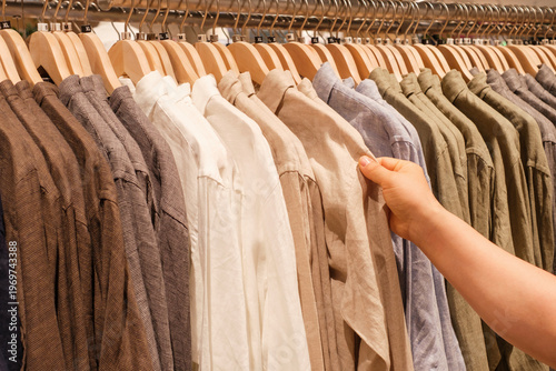 Man chooses a shirt hanging on hanger in store, side view.