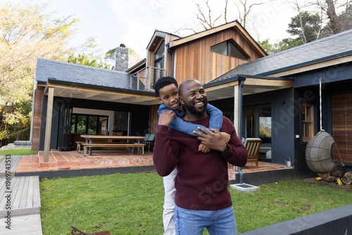African American father and son playing, father carrying child on back near wooden house patio